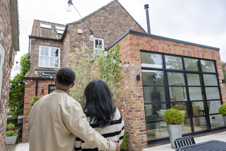Couple in back garden looking at house, man with arm around woman, home improvement, building, extension, house purchase