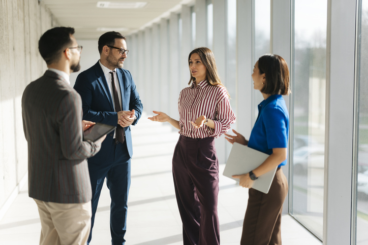 Four diverse business professionals collaborating, communicating, and discussing ideas in a bright office corridor